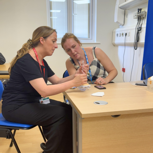Natalie and Phoebe sit at a desk during a medical demonstration session, looking at a syringe together.